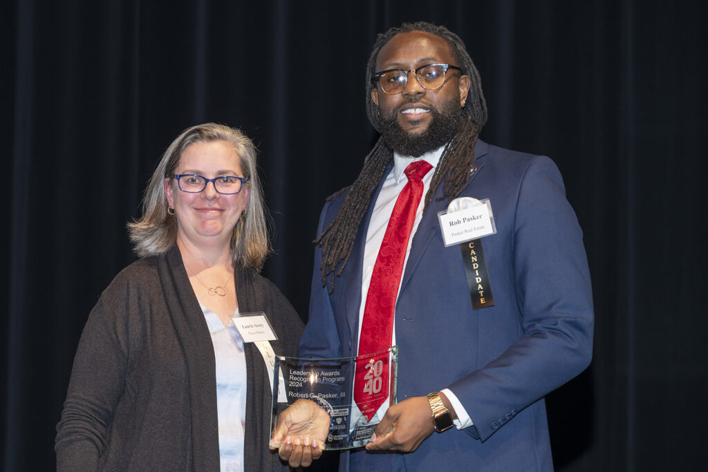 Rob Pasker smiling in front of a 20 Under 40 banner after receiving his award for civic leadership and community impact in Toledo.